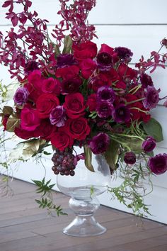 a vase filled with red and purple flowers sitting on top of a wooden floor next to a white wall