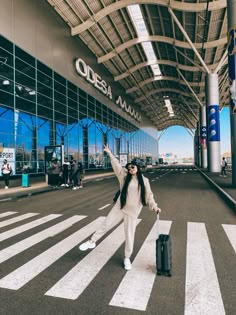 a woman is standing in an airport with her arms up and luggage on the ground