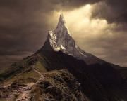 a very tall mountain with a snow capped peak in the distance under a cloudy sky