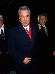 an older man in a suit and tie standing next to other men with umbrellas