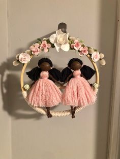 two black dolls in pink dresses are hanging on a door hanger with flowers and leaves