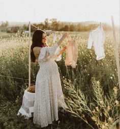 a woman in a white dress hanging out clothes on a line and looking at the sky