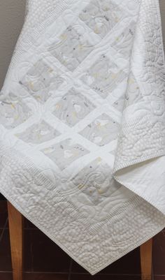 a white quilted blanket sitting on top of a wooden chair