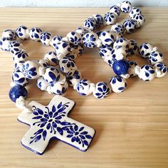 a wooden table topped with blue and white ceramic beads next to a small cross pendant