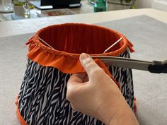 a person cutting fabric with scissors on a table in front of a vase and other items