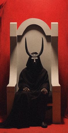 a person sitting in a chair with a horned head on it's face and wearing a black cloak