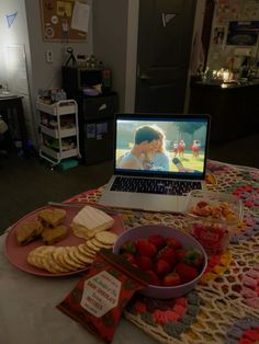 a laptop computer sitting on top of a table filled with fruit and crackers next to a bowl of strawberries