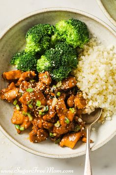 a bowl filled with rice and broccoli covered in sauce next to a spoon