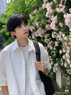 a young man standing next to a bush with pink flowers on it's side