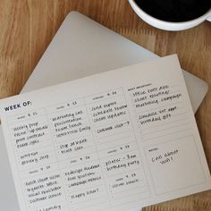 a cup of coffee sitting next to an open notebook on top of a wooden table