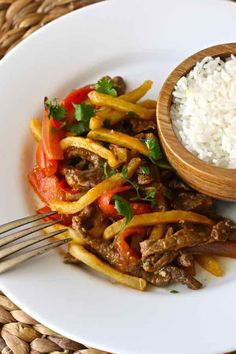 a white plate topped with stir fry and rice next to a wooden bowl filled with meat