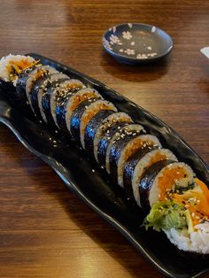 a black plate topped with sushi on top of a wooden table