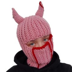 a young boy wearing a knitted pink devil mask with horns on it's head