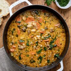 a pot filled with soup sitting on top of a wooden table next to some bread