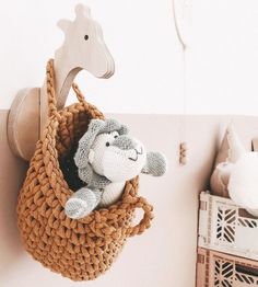 a stuffed animal in a crocheted basket hanging from a hook on the wall