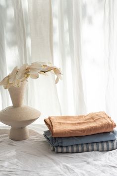 a white vase sitting on top of a bed next to two folded towels and a flower