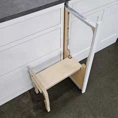 a wooden step stool sitting in front of a kitchen counter next to a white wall