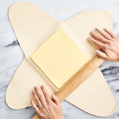 two hands rolling out dough on top of a pizza board with a wooden spatula