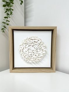 a wooden frame with a white flower in it on a table next to a potted plant