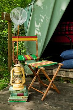 a chair and some books on a wooden deck in front of a tent with trees