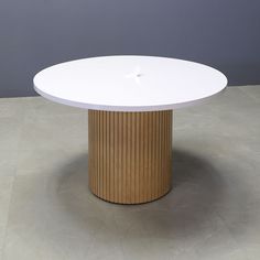 a round white table sitting on top of a cement floor next to a gray wall