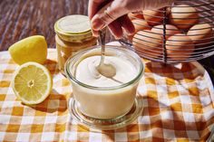 a person spooning mayonnaise into a jar with lemons and eggs in the background