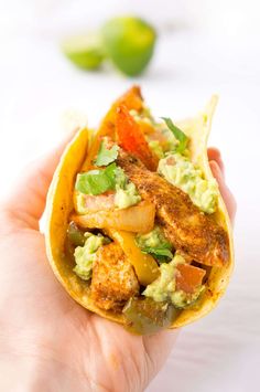 a hand holding a taco filled with chicken and guacamole