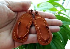 a person holding two leather flip flops in their hand with green plants behind them