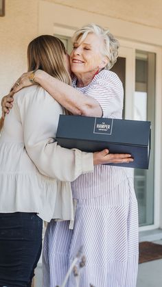 two women hugging each other and holding a box