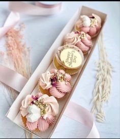 four cupcakes in a box with pink ribbons and flowers on the top one