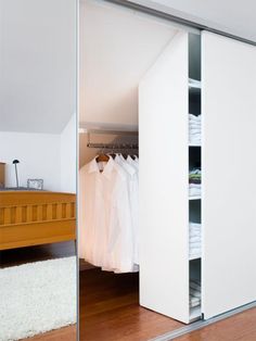 an open closet with clothes hanging on hangers and a bed in the corner next to it