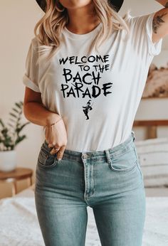 a woman wearing a white shirt and jeans with a hat on her head is standing in front of a bed