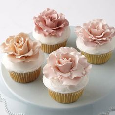 four cupcakes with pink frosting and flowers on them sitting on a plate