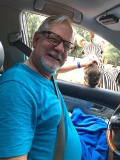 a man sitting in the driver's seat of a car next to a zebra