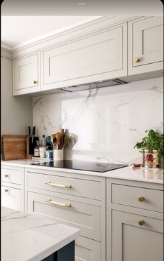 a kitchen with white cabinets and marble counter tops, gold pulls on the cabinet doors