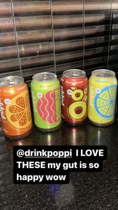 four cans of soda sitting on top of a counter next to a window with the words drinkpopi i love these my guts so happy wow