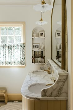 a bathroom with marble counter top and white walls, along with a gold framed mirror