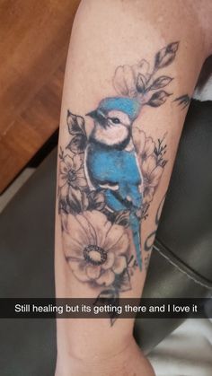 a blue bird sitting on top of a woman's leg with flowers around it