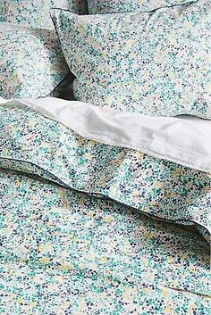 an unmade bed with blue and green flowers on the comforter, pillows and sheets