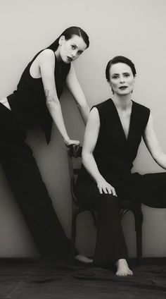 two women sitting on chairs in black and white pose for the camera with their legs crossed