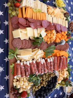 an assortment of cheeses, meats and fruits on a platter with american flag background