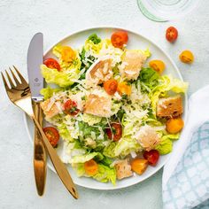 a white plate topped with lettuce, tomatoes and croutons next to a fork