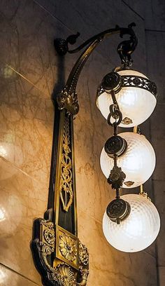 an ornate light fixture hanging from the side of a wall with three lights on it