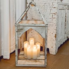 four lit candles sit in an old, white frame on the floor next to a window