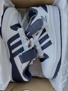 a pair of white and blue adidas sneakers in a box with the shoe laces down