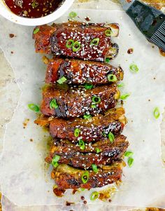 ribs covered in sauce and green onions on parchment paper next to a bowl of dipping sauce