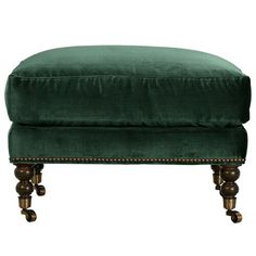 a green velvet ottoman with wooden legs and studdings on the bottom, sitting in front of a white background