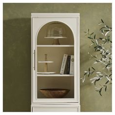 a white bookcase with glass doors and shelves in front of a vase filled with flowers