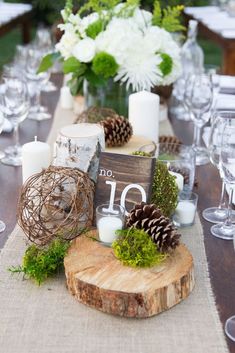 the table is set with candles, pine cones and greenery for an elegant centerpiece