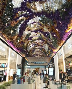 the inside of a shopping mall with people walking around and flowers hanging from the ceiling